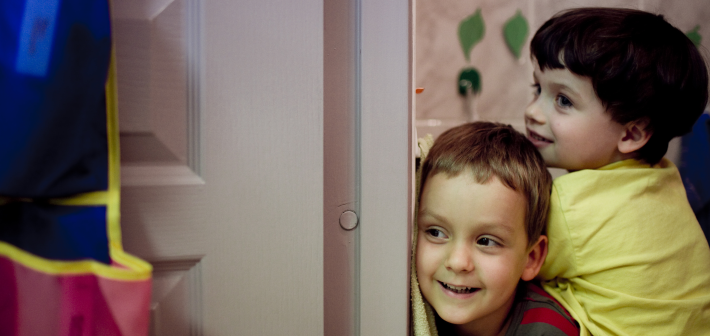 Dwójka uśmiechniętych dzieci zerka zza drzwi